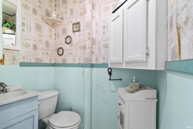 half bath with wallpapered walls, vanity, and toilet
