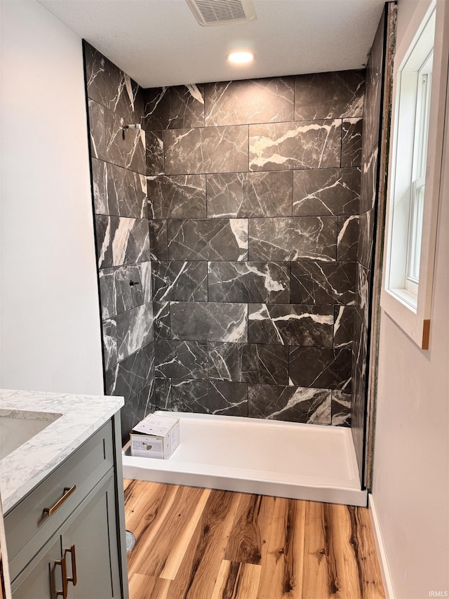 full bath with recessed lighting, tiled shower, vanity, visible vents, and wood finished floors