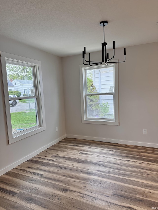 unfurnished dining area with baseboards, wood finished floors, a notable chandelier, and plenty of natural light