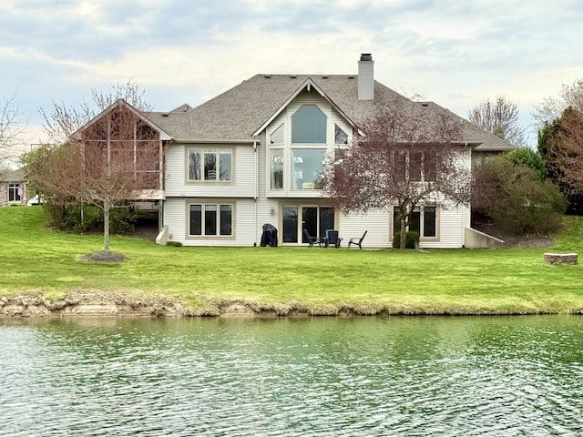 back of house with a lawn, a chimney, roof with shingles, and a water view