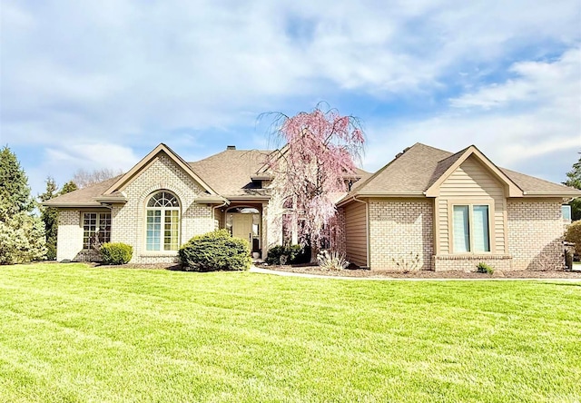 view of front of home with brick siding, roof with shingles, and a front yard