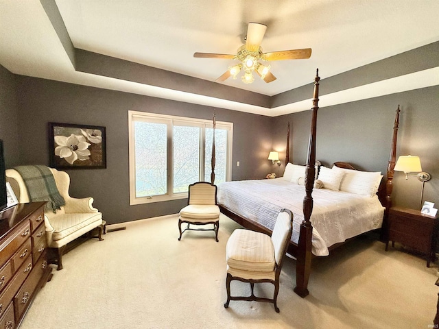 bedroom featuring light carpet, a ceiling fan, a tray ceiling, and baseboards