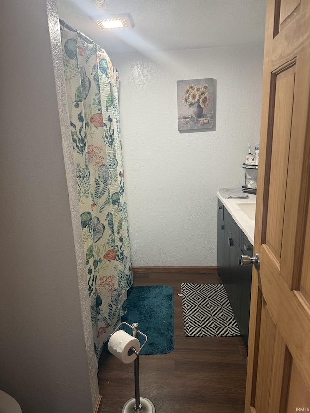 bathroom with a shower with shower curtain, baseboards, wood finished floors, and vanity