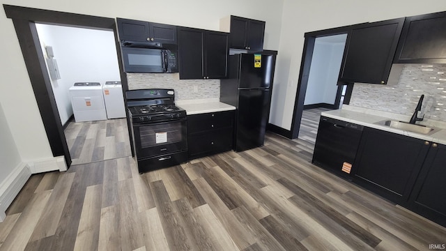 kitchen with washing machine and clothes dryer, a sink, black appliances, dark cabinetry, and light countertops