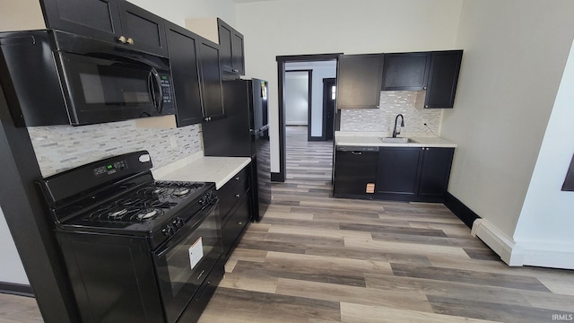 kitchen with a sink, black appliances, dark cabinetry, light wood finished floors, and light countertops