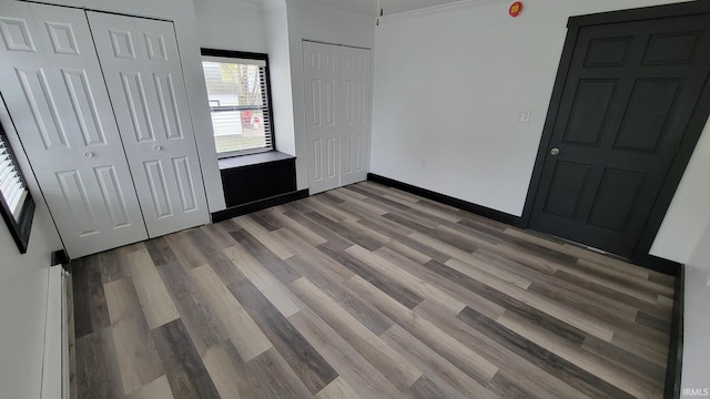 unfurnished bedroom featuring baseboards, crown molding, wood finished floors, and multiple closets