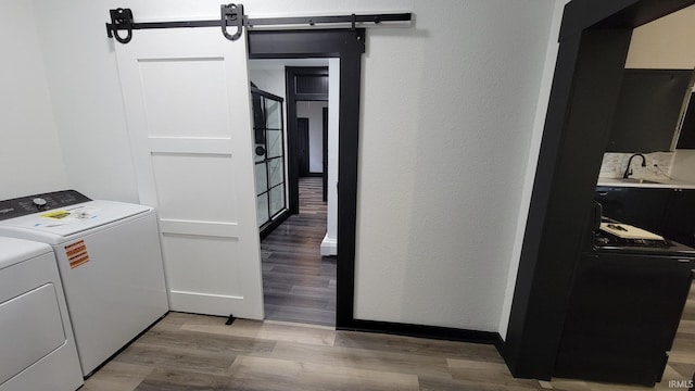 laundry room with a barn door, a sink, separate washer and dryer, light wood-style floors, and laundry area