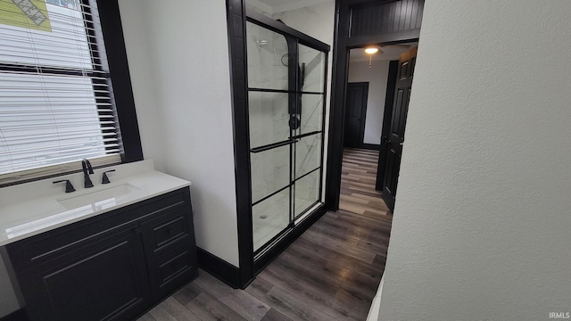 bathroom with a textured wall, vanity, wood finished floors, and a walk in shower