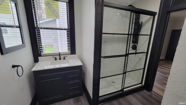 bathroom with a textured wall, vanity, wood finished floors, and a shower stall