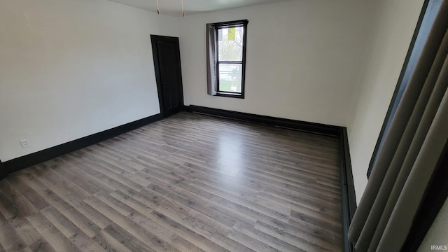 spare room with baseboards and dark wood-type flooring