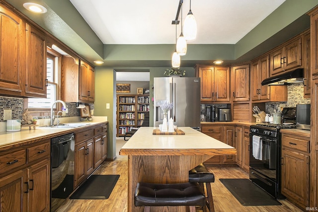 kitchen featuring under cabinet range hood, a sink, a center island, decorative backsplash, and black appliances