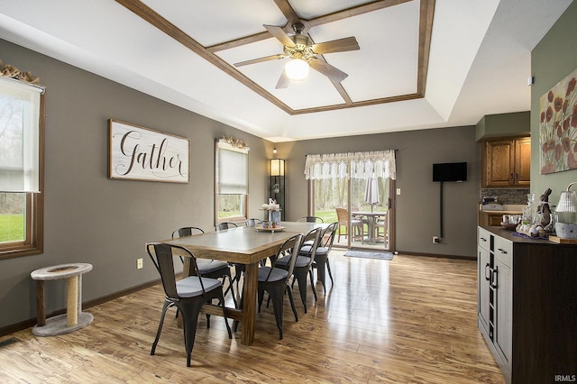 dining room with a raised ceiling, light wood-style flooring, baseboards, and ceiling fan