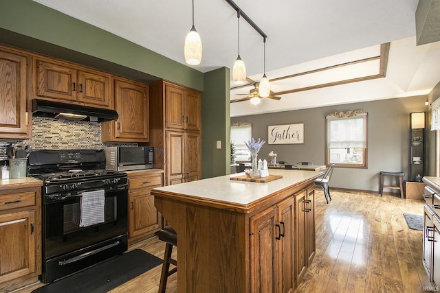kitchen featuring tasteful backsplash, brown cabinetry, black range with gas stovetop, under cabinet range hood, and a kitchen island