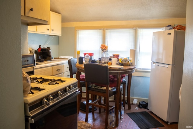 kitchen featuring white cabinets, freestanding refrigerator, baseboards, gas stove, and light countertops