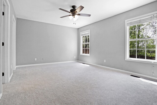 unfurnished room with ceiling fan, carpet floors, visible vents, and plenty of natural light