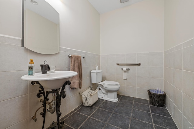half bath featuring tile walls, wainscoting, tile patterned flooring, and toilet