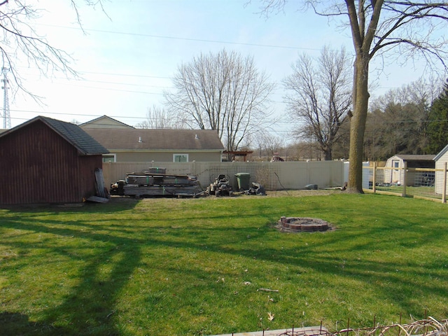 view of yard with a fenced backyard, a fire pit, a storage shed, and an outbuilding