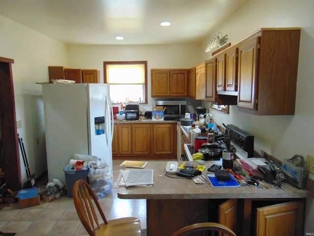 kitchen with stainless steel microwave, light tile patterned flooring, a peninsula, white fridge with ice dispenser, and brown cabinetry