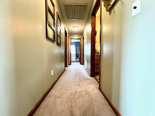 corridor featuring attic access, a textured ceiling, light carpet, and visible vents
