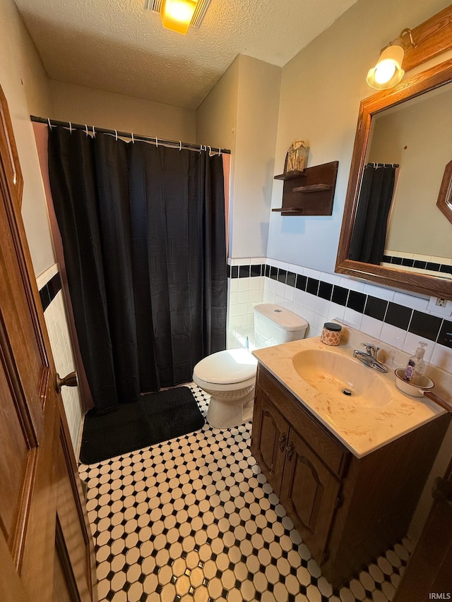 bathroom with a wainscoted wall, a textured ceiling, toilet, a shower with shower curtain, and vanity