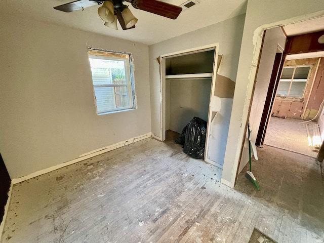 unfurnished bedroom with a closet, hardwood / wood-style flooring, ceiling fan, baseboards, and visible vents