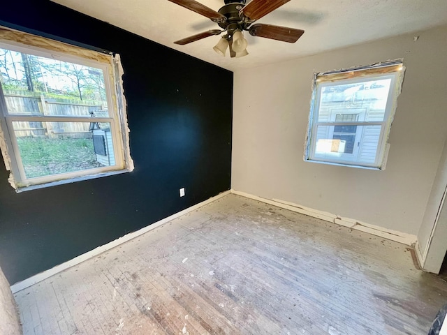 spare room with wood finished floors, a ceiling fan, and baseboards