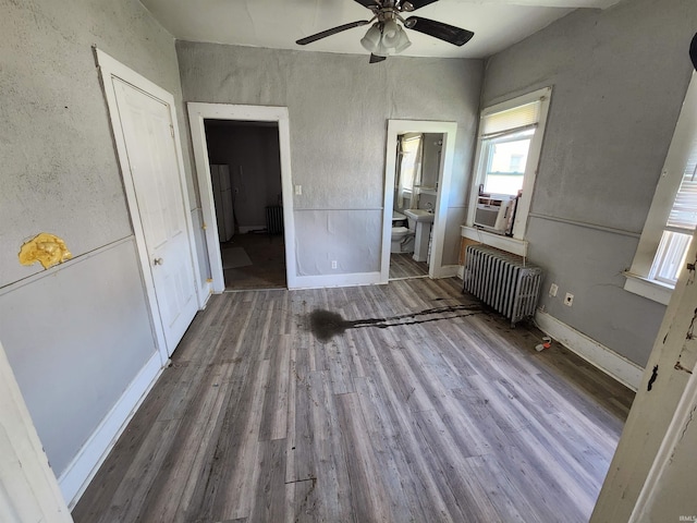unfurnished bedroom featuring radiator, ensuite bath, wood finished floors, and cooling unit