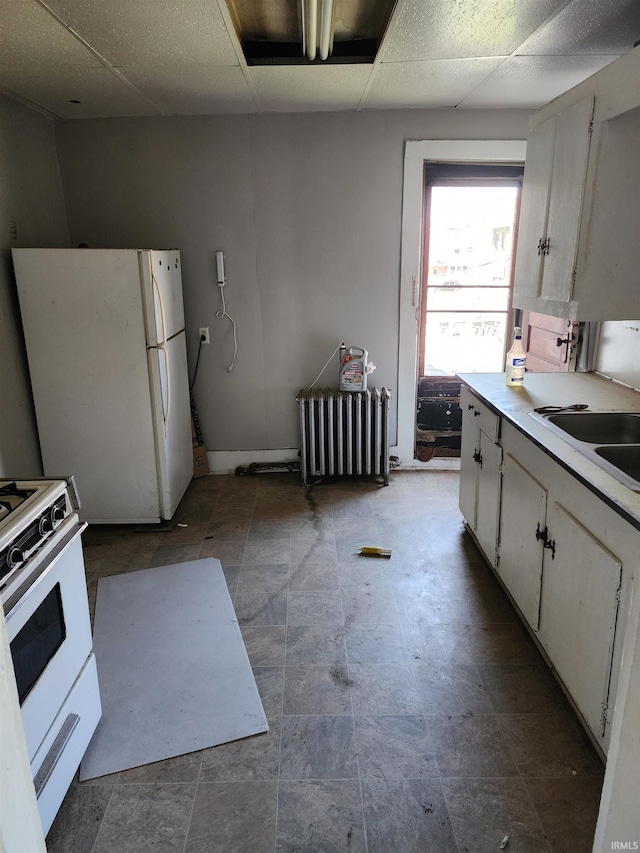 kitchen featuring white cabinets, a sink, radiator heating unit, white appliances, and light countertops