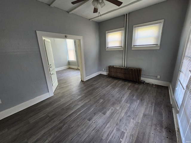 empty room featuring dark wood-type flooring, radiator heating unit, a healthy amount of sunlight, and a ceiling fan