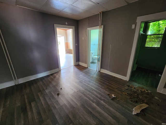 empty room with dark wood-type flooring, a drop ceiling, and baseboards