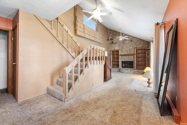 stairs featuring a textured ceiling, carpet floors, vaulted ceiling, ceiling fan, and a fireplace