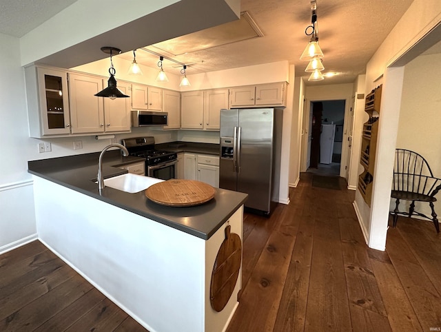 kitchen with a peninsula, dark countertops, stainless steel appliances, and a sink