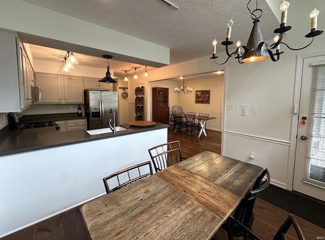 kitchen with dark wood finished floors, dark countertops, a peninsula, a chandelier, and stainless steel fridge