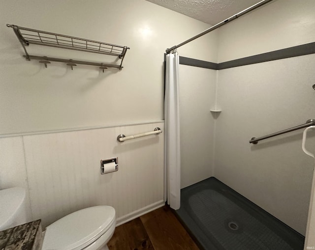 full bath featuring a textured ceiling, toilet, wainscoting, a stall shower, and wood finished floors