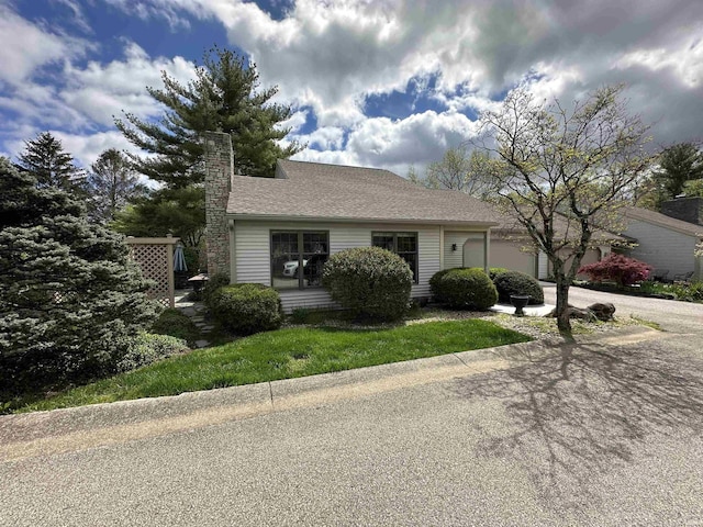 view of front of house with driveway, a chimney, roof with shingles, and a garage