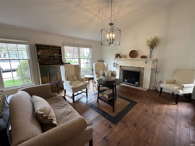 living room featuring dark wood finished floors, vaulted ceiling, a stone fireplace, and an inviting chandelier