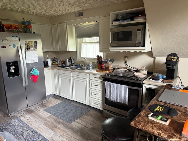 kitchen featuring wood finished floors, a sink, white cabinets, appliances with stainless steel finishes, and visible vents