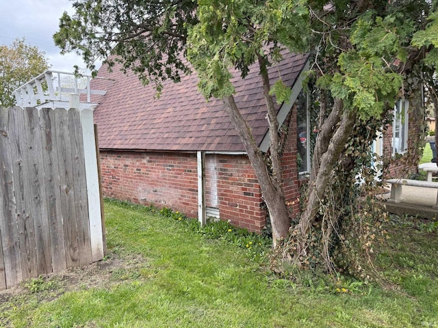 view of side of home with roof with shingles, brick siding, and a yard