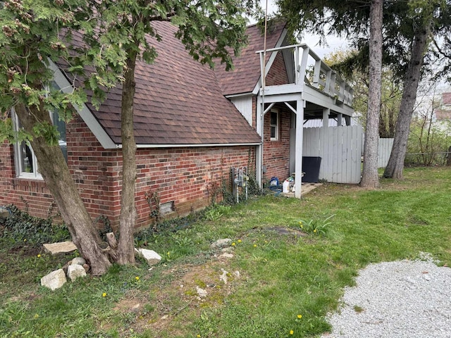 view of side of property featuring brick siding, a yard, roof with shingles, and fence