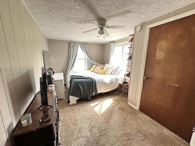 bedroom featuring wooden walls, a textured ceiling, carpet flooring, and a ceiling fan
