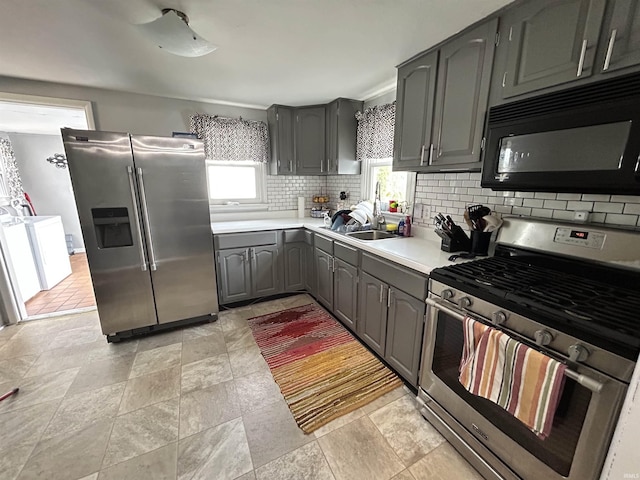 kitchen featuring stainless steel appliances, light countertops, gray cabinets, a sink, and tasteful backsplash