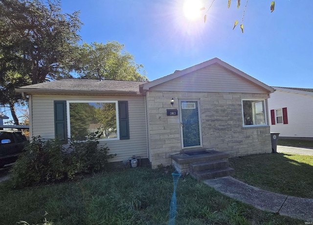 bungalow featuring stone siding, roof with shingles, and a front yard