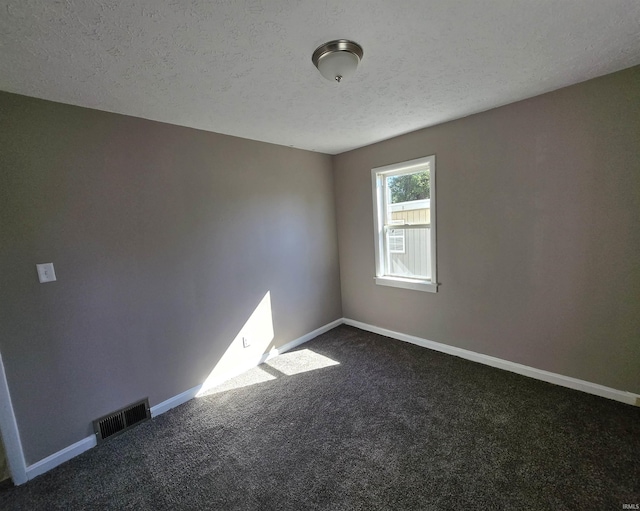 empty room with baseboards, visible vents, dark carpet, and a textured ceiling