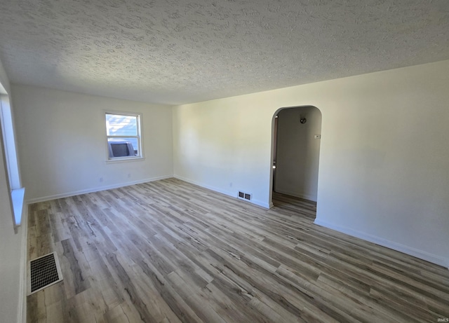 spare room featuring arched walkways, visible vents, wood finished floors, and a textured ceiling