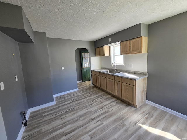 kitchen with arched walkways, light wood finished floors, baseboards, and a sink