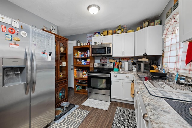 kitchen with dark wood-style flooring, white cabinetry, light stone countertops, and stainless steel appliances