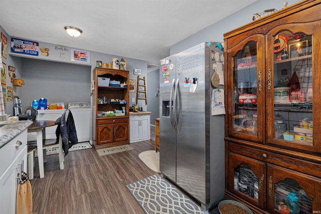 kitchen with stainless steel refrigerator with ice dispenser, washer / clothes dryer, dark wood-type flooring, and light countertops
