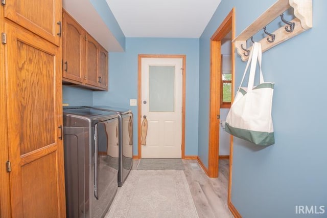 washroom featuring washing machine and clothes dryer, baseboards, light wood-type flooring, and cabinet space