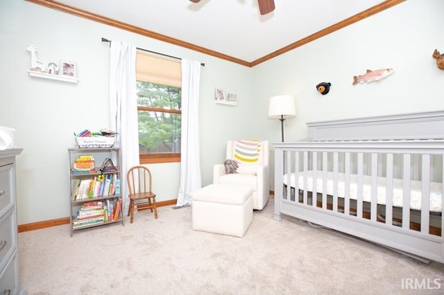 bedroom featuring a crib, ornamental molding, baseboards, carpet flooring, and ceiling fan