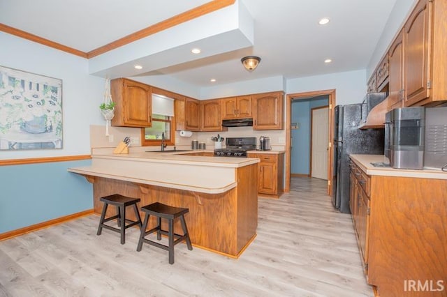 kitchen featuring brown cabinets, under cabinet range hood, black stove, a peninsula, and a breakfast bar area
